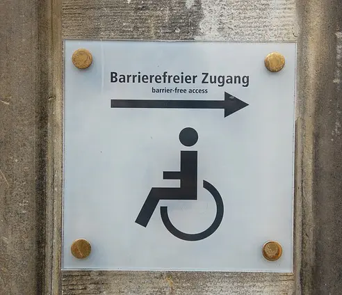 Türschild mit einem Pfeil nach rechts und einem Rollstuhlfahrer-Icon. Beschriftung: Barrierefreier Zugang