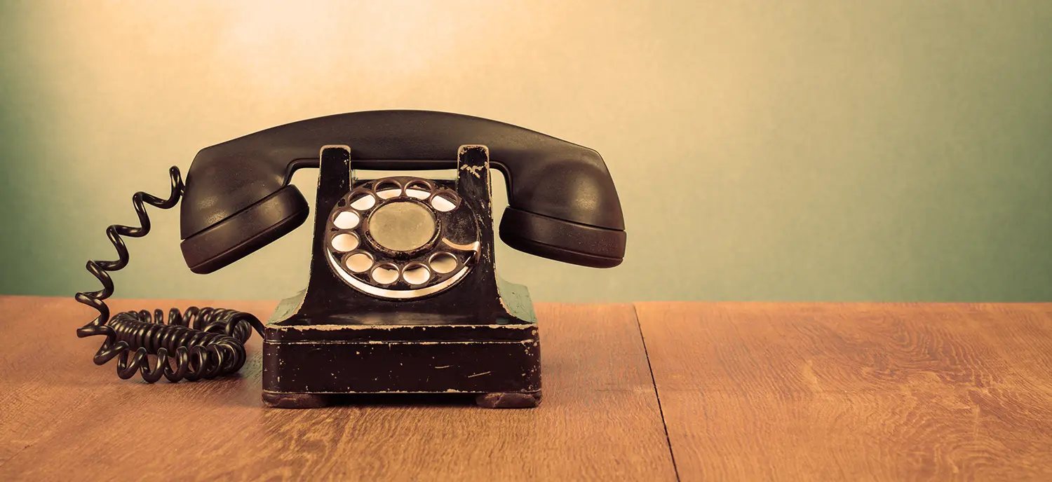 Ein altes schwarzes kabelgebundenes Telefon mit Wählscheibe auf einem Holztisch