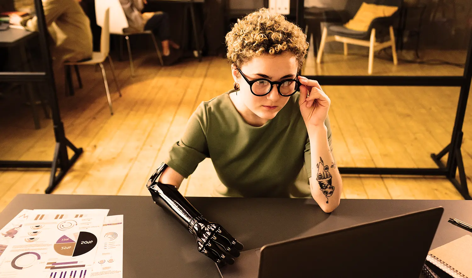 junge Frau, kurze Haare, Brille, Armprothese sieht in einen Laptop